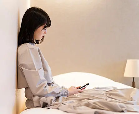 ベッドに座ってスマートフォンを見る女性