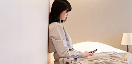 ベッドに座ってスマートフォンを見る女性